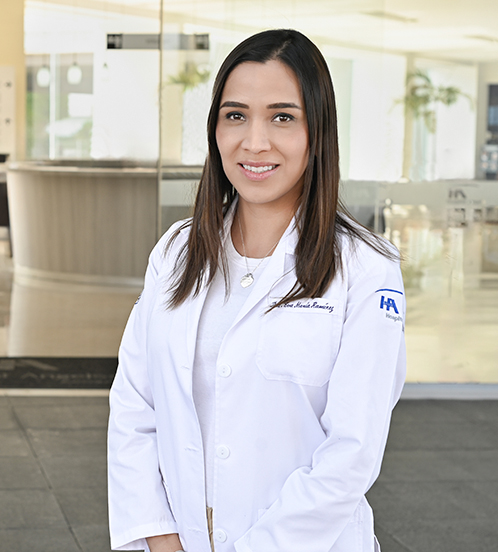Es la foto de perfil de una cirujana general en Ciudad de México de Hospital Angeles Acoxpa. Usa un abata color blanco, junto con una blusa blanca y pantalon color cafe claro. Tiene el cabello café y lacio.