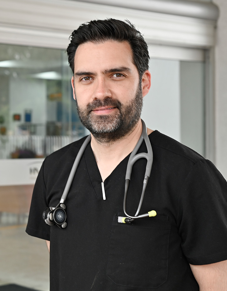Es la foto de perfil de un cardiólogo intervencionista en Tijuana de Hospital Angeles Tijuana. Tiene el cabello y barba negro. Usa una camisa azul oscuro.