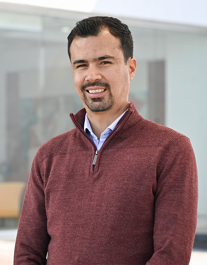 Es la foto de perfil de un neurólogo pediátrico en Tijuana de Hospital Angeles Tijuana. Usa un sueter rojo con una camisa azul claro. Tien el cabello y barba negra.
