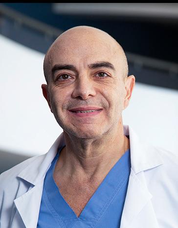 Es la foto de perfil de un ortopedista y traumatólogo en Huixquilucan de Hospital Angeles Lomas. Usa una bata blanca con una playera azul, tiene cejas pobladas y está sonriendo.