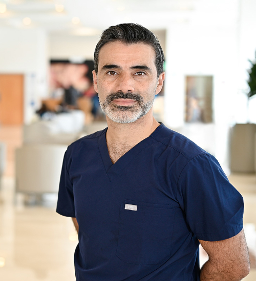 Es la foto de perfil de un ginecólogo y obstetra en Xalapa de Hospital Angeles Xalapa. Usa una bata blanca con un uniforme médico azul. Tiene el cabello y barba negra.