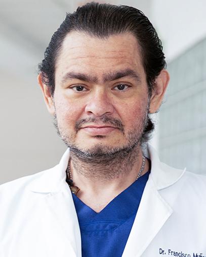 Es la foto de perfil de un cirujano general en Huixquilucan de Hospital Angeles Lomas. Usa una bata blanca con un uniforme azul, el cabello oscuro y barba canosa.