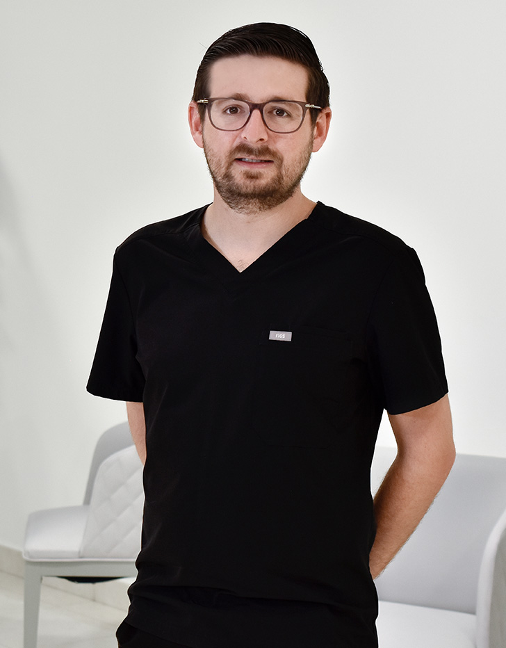 Es la foto de perfil de un gastrocirujano en Huixquilucan, Estado de México de Hospital Angeles Lomas. Usa un uniforme médico color negro. Tiene el cabello y barba café. Usa lentes cafés.
