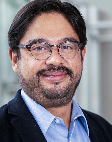 Es la foto de perfil de un urólogo en Huixquilucan de Hospital Angeles Lomas. Usa un traje negro con camisa azul, tiene lentes y está sonriendo.