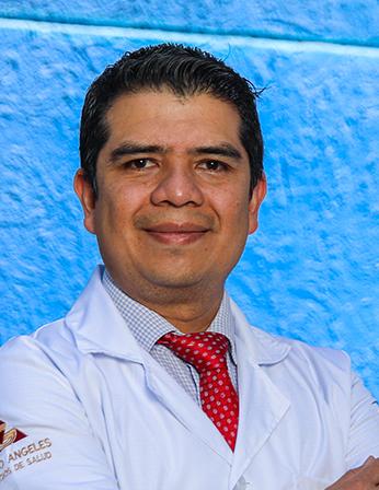 Es la foto de perfil de un urólogo en León de Hospital Angeles León. Usa una bata blanca con camisa azul claro y una corbata, tiene los brazos cruzados y está sonriendo.