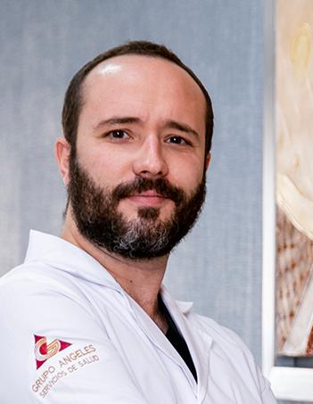 Es la foto de perfil de un urólogo en León de Hospital Angeles León. Usa una bata blanca, tiene los brazos cruzados y usa barba y bigote.