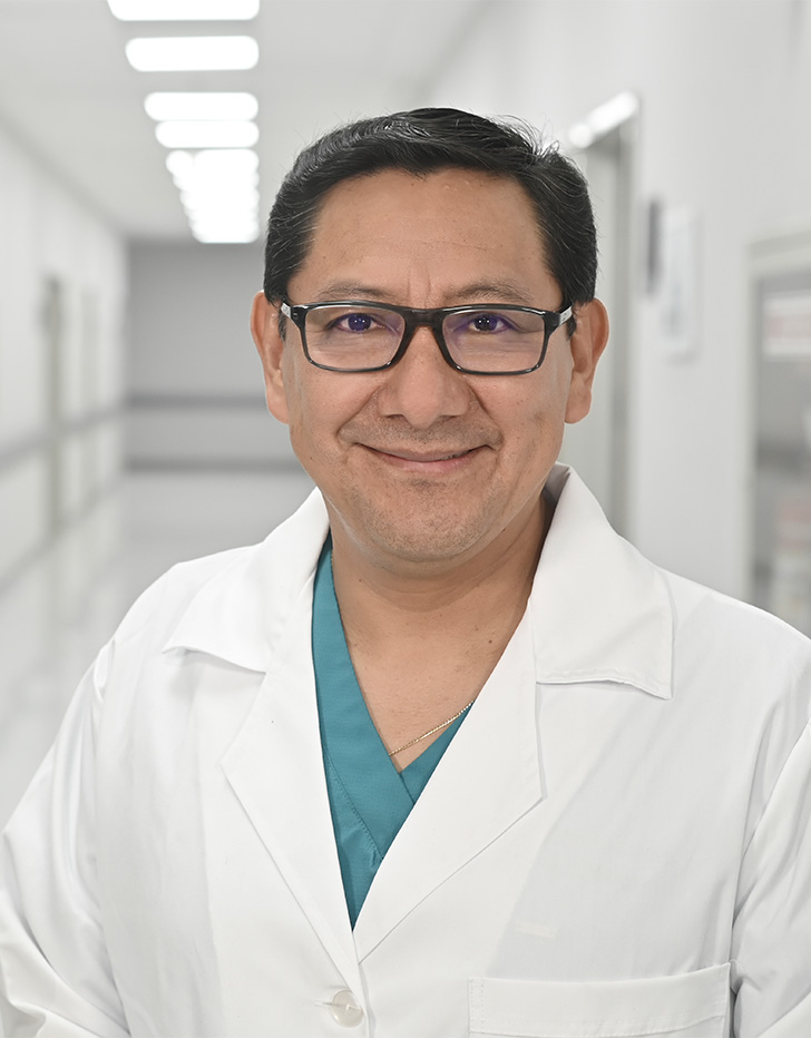 Es la foto de perfil de un oftalmólogo en Ciudad de México de Hospital Angeles Universidad. Usa una bata blanca y un uniforme médico de color azul claro. Tiene el cabello negro y lentes. Está sonriendo.