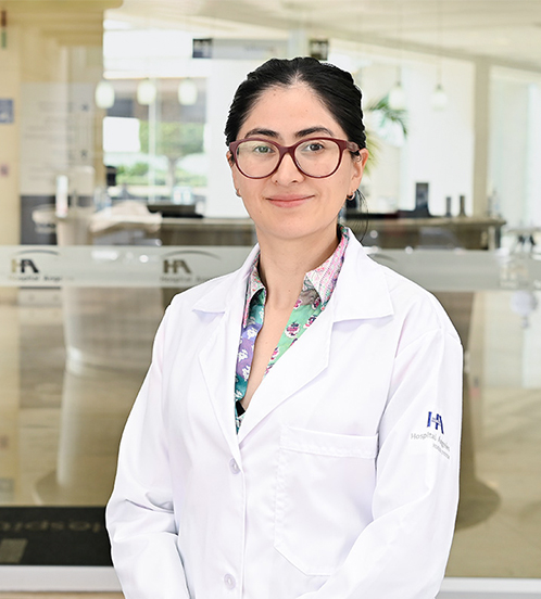 Es la foto de perfil de una cirujana oncóloga en Ciudad de México de Hospital Angeles Acoxpa. Usa una bata blanca con una blusa rosa con azul y flores. Tiene el cabello recogido y usa lentes vino.