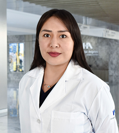 Es la foto de perfil de una oftalmóloga en Querétaro de Hospital Angeles Centro-sur. Usa una bata blanca y un uniforme médico color negro. Usa un collar con varios dijes de color dorado. Tiene el cabello largo y café.