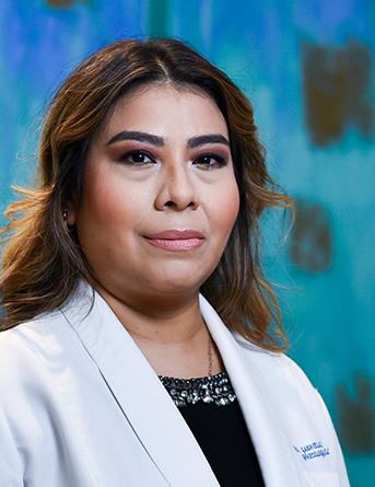 Es la foto de perfil de una ginecóloga y obstetra en Villahermosa de Hospital Angeles Villahermosa. Usa una bata blanca y una blusa negra. Tiene el cabello largo color castaño.