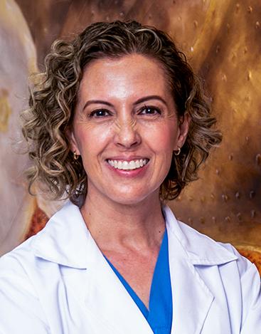 Es la foto de perfil de una cirujana maxilofacial en León de Hospital Angeles León. La doctora tiene el cabello rizado castaño con luces rubias. está sonriendo amablemente.