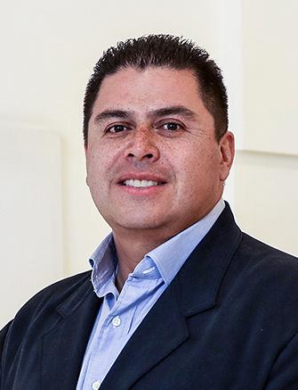 Es la foto de perfil de un cirujano plástico en León de Hospital Angeles León. Viste un saco negor con una camisa azul cielo, está sonriendo.