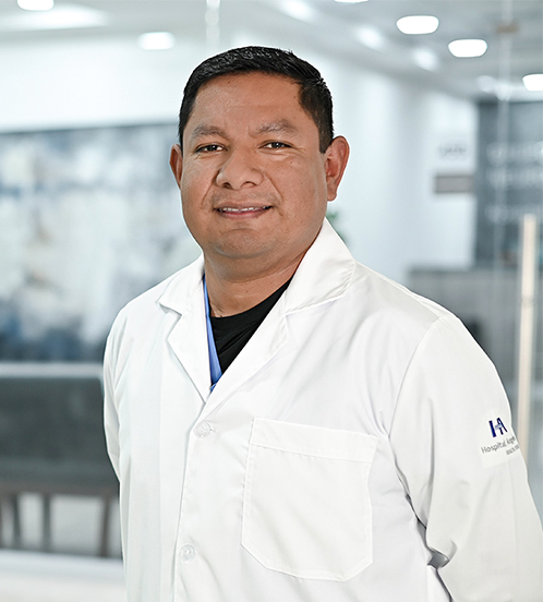 Es la foto de perfil de un neumólogo en Ciudad de México de Hospital Angeles Acoxpa. Usa una bata blanca con un uniforme médico color azul claro y una playera negra. Tiene el cabello café oscuro y los brazos cruzados por detrás.
