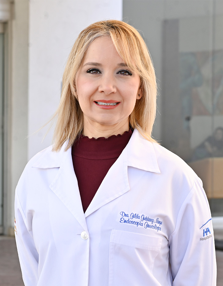 Es la foto de perfil de una ginecóloga y obstetra en Tijuana de Hospital Angeles Tijuana. Usa una bata blanca con un sueter rojo. Tiene el cabello largo y rubio.