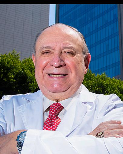 Es la foto de perfil de un cirujano neurológico en Ciudad de México de Hospital Angeles Pedregal. Usa una bata y camisa blanca con una corbata roja. Está sonriendo y tiene los brazos cruzados.