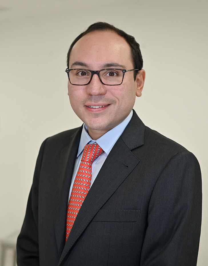 Es la foto de perfil de un coloproctólogo y especialista en cirugía general en Ciudad de México de Hospital Angeles Clínica Londres. Usa un uniforme azul y de fondo se ve el hospital. 