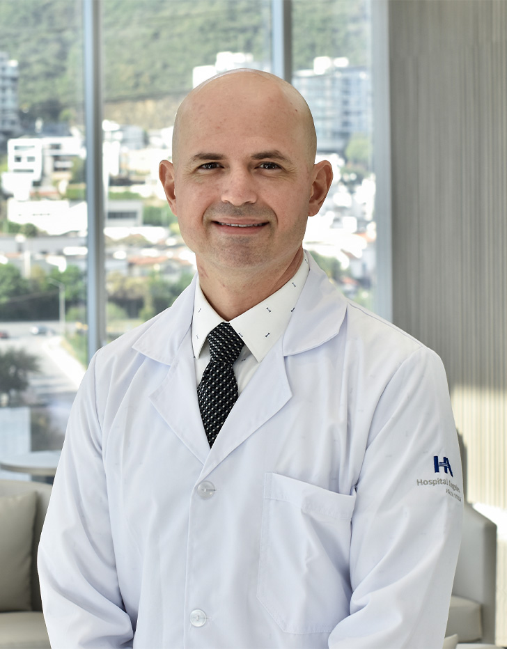Es la foto de perfil de un otorrinolaringólogo en San Pedro Garza de Hospital Angeles Valle Oriente. Usa una bata y camisa blanca con una corbata café. Está sonriendo.