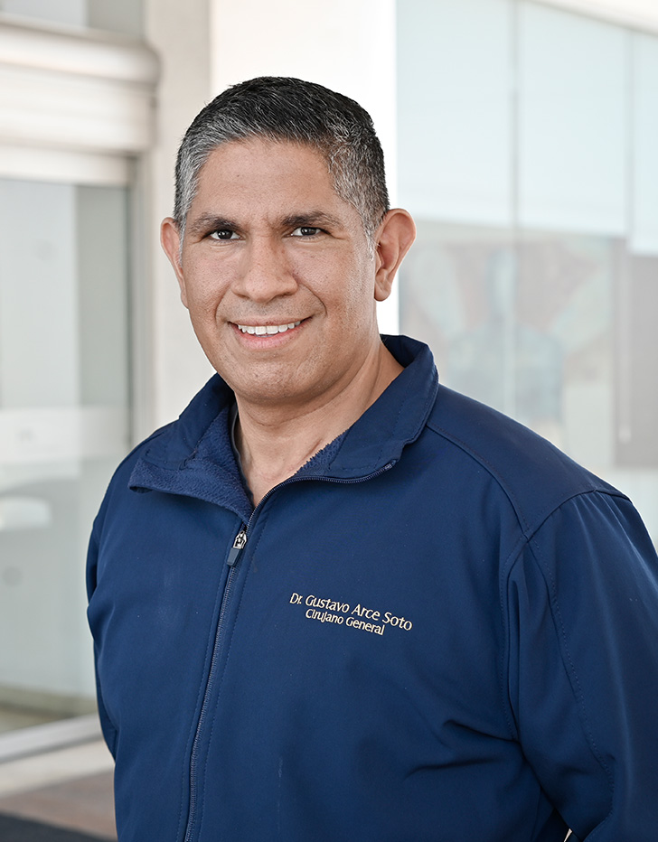 Es la foto de perfil de un cirujano general en Tijuana de Hospital Angeles Tijuana. Usa una chamarra azul. Tiene el cabello gris y está sonriendo.
