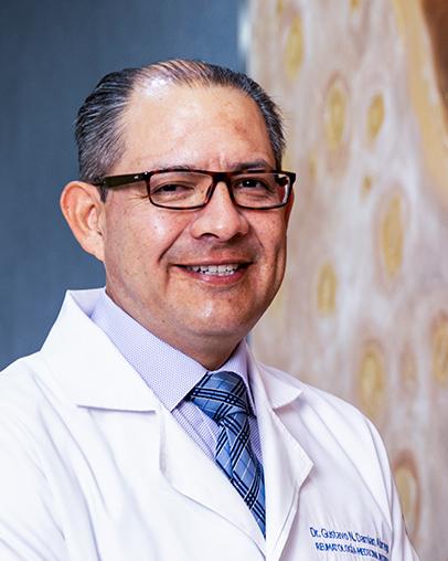 Es la foto de perfil de un reumatólogo en León de Hospital Angeles León. Usa una bata blanca, tiene una camisa lila, corbata azul y lentes.