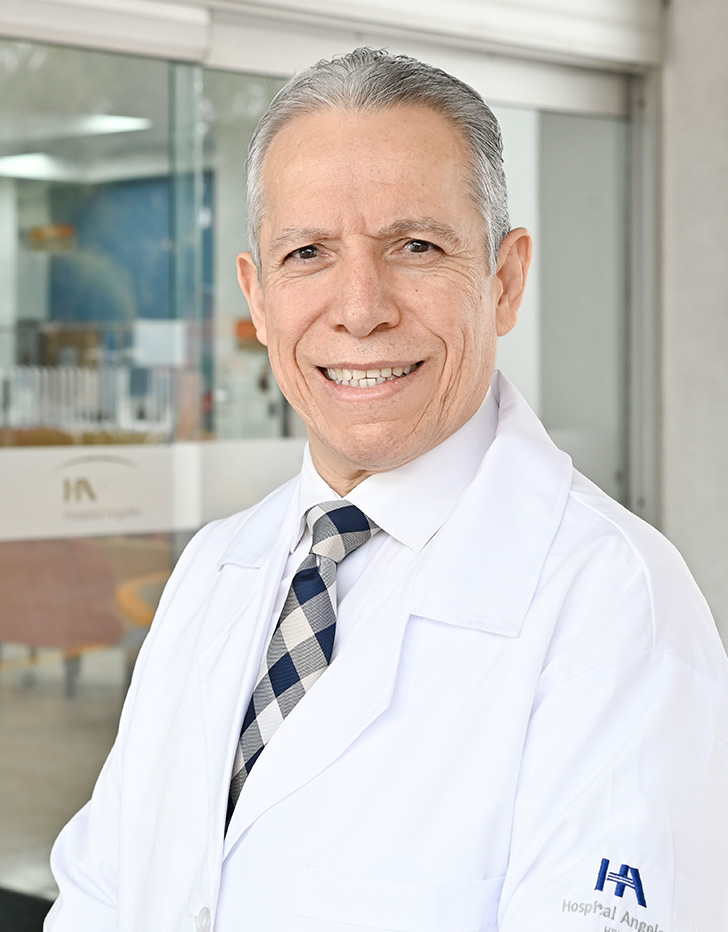 Es la foto de perfil de un pediatra y cirujano pediátrico en Tijuana de Hospital Angeles Tijuana. Usa una bata blanca con una camisa azul claro y corbata azul fuerte. Tiene el cabello gris y está sonriendo.
