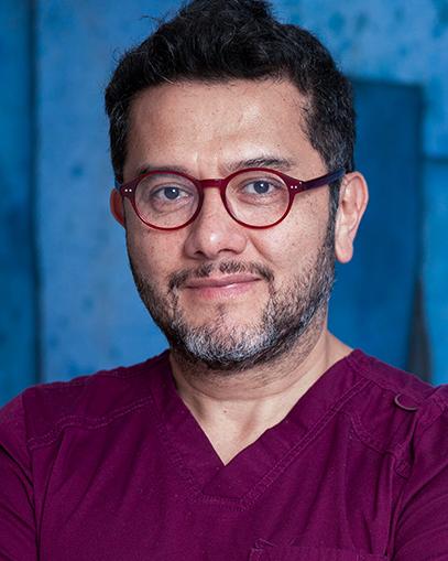 Es la foto de perfil de un cirujano plástico en Huixquilucan de Hospital Angeles Lomas. Usa un uniforme de color vino, tiene lentes y el marco de los lentes es rojo.