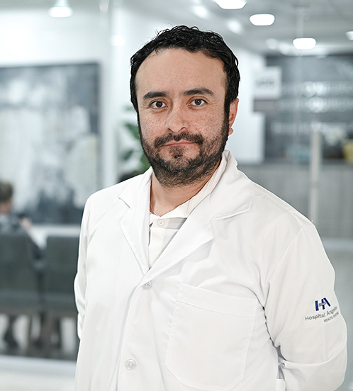 Es la foto de perfil de un cirujano neurológico en Ciudad de México de Hospital Angeles Acoxpa. Usa una bata blanca con una camisa blanca. Tiene barba y cabelo negro.