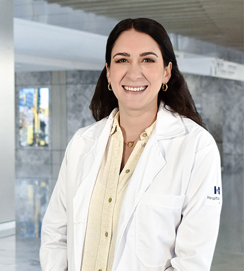 Es la foto de perfil de una pediatra en Querétaro de Hospital Angeles Centro-sur. Tiene puesta una bata blanca con una camisa color amarillo claro. Usa joyería color dorado. Tiene el cabello largo y café oscuro.