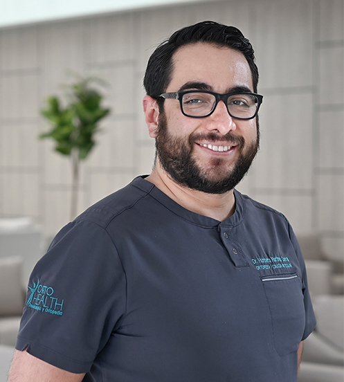 Es la foto de perfil de un cirujano general en Querétaro de Hospital Angeles Centro Sur. está sonriendo, viste un uniforme gris con letras bordadas azules, tiene barba y lentes con marco negro.
