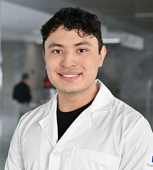 Es la foto de perfil de un odontólogo en Querétaro de Hospital Angeles Centro-sur. Tiene el cabello negro y chino. Usa una bata blanca con una playera negra. Está sonriendo.