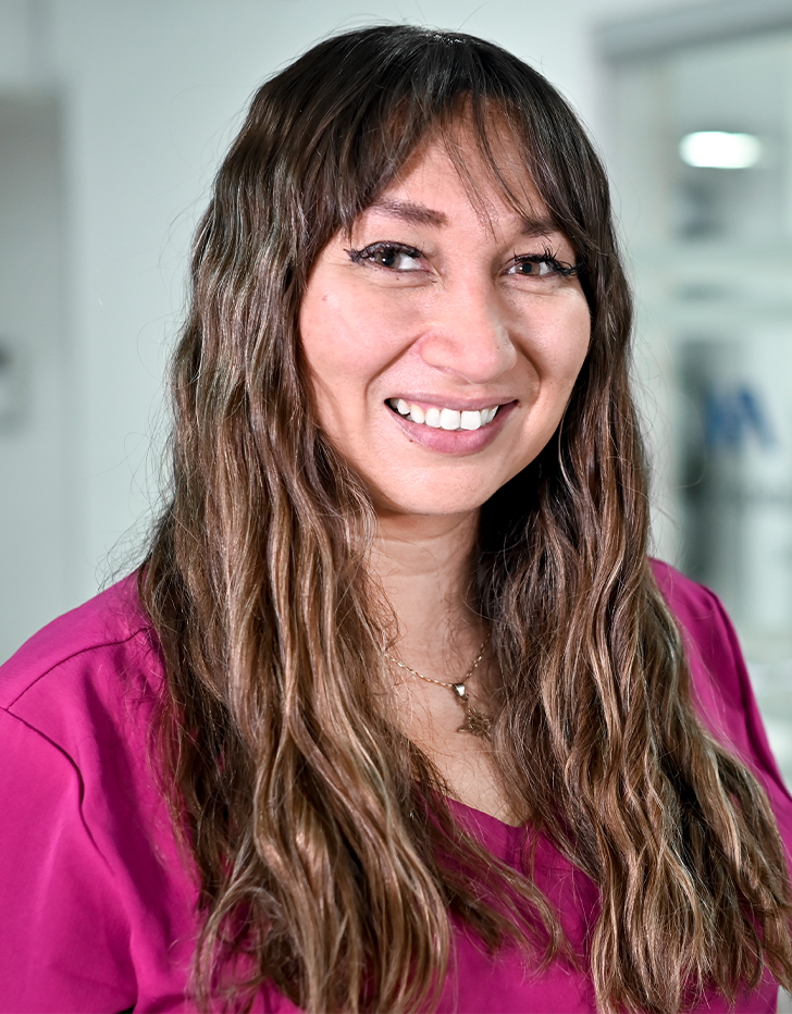 Es la foto de perfil de una neuróloga en Ciudad de México de Hospital Angeles Santa Mónica. Usa un uniforme médico rosa. Tiene el cabello largo y ondulado. Está sonriendo.