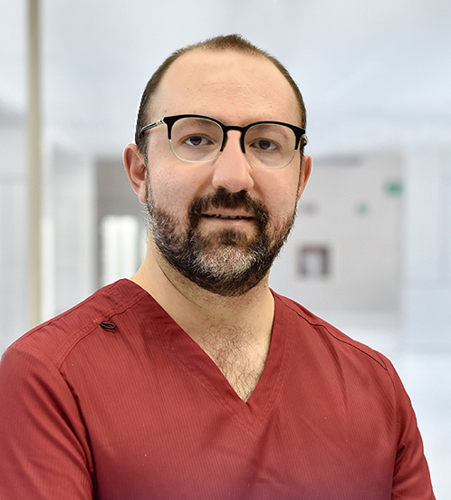 Es la foto de perfil de un cirujano pediátrico en Querétaro de Hospital Angeles Centro Sur. Viste un uniforme de color ladrillo, tiene barba y lentes.