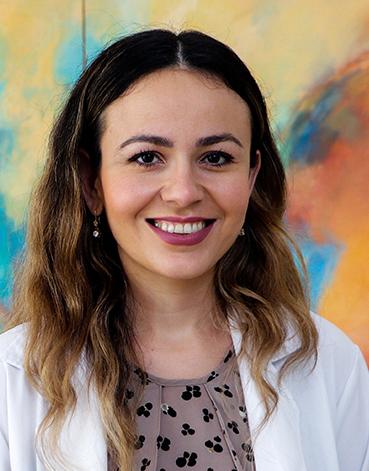 Es la foto de perfil de una dermatóloga pediátrica en Tampico de Hospital Angeles Tampico. Usa una bata blanca y una blusa café con estampados negros. Tiene el cabello ondulado y castaño. Está sonriendo.