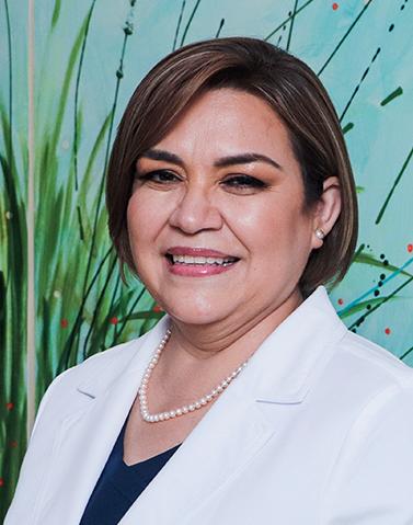Es la foto de perfil de una ginecóloga y obstetra en Tampico de Hospital Angeles Tampico. Usa una bata blanca, blusa azul y un collar. Tiene el cabello corto y café.