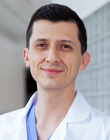 Es la foto de perfil de un oftalmólogo en Huixquilucan de Hospital Angeles Lomas. Utiliza una bata blanca con un uniforme de color azul, es de tez clara y está sonriendo.