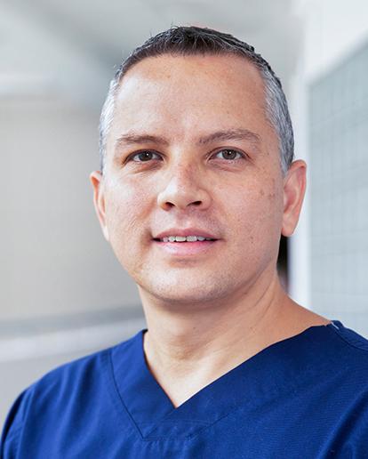 Es la foto de perfil de un pediatra especialista en cirugía pediátrica en Huixquilucan de Hospital Angeles Lomas. El doctor usa un uniforme médico azul, tiene el cabello corto y canoso. 