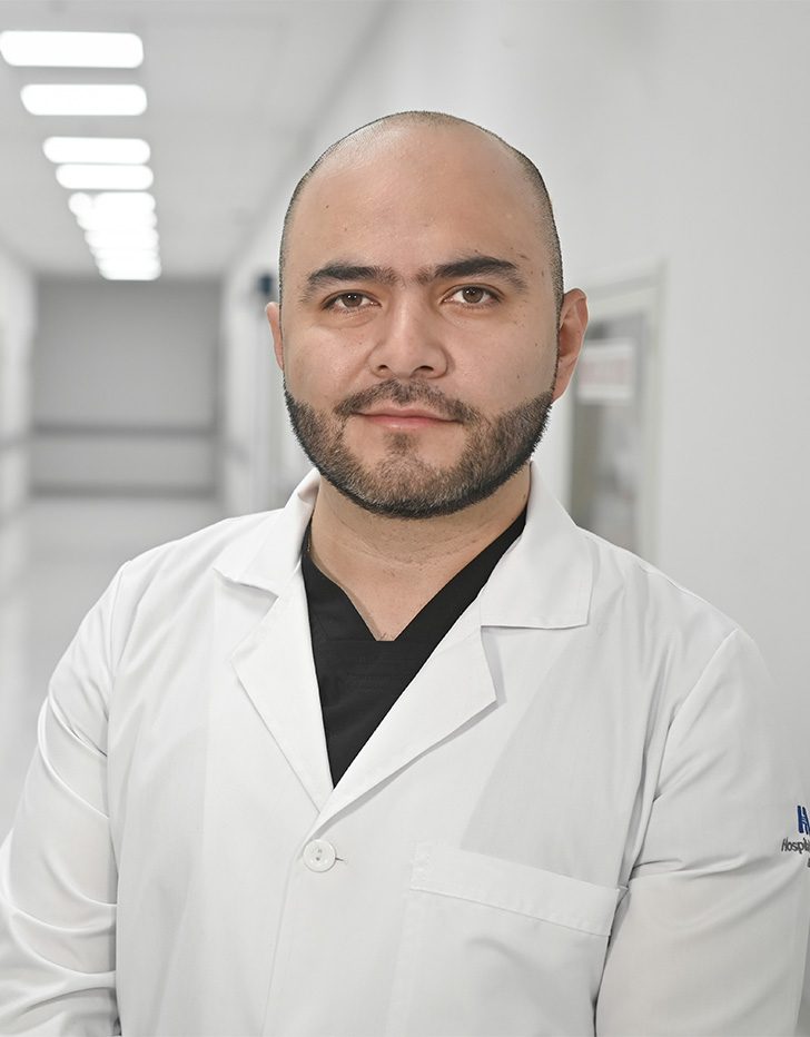 Es la foto de perfil de un cirujano maxilofacial en Ciudad de México de Hospital Angeles Universidad. Usa una bata blanca con un uniforme médico negro. Tiene la barba negra.