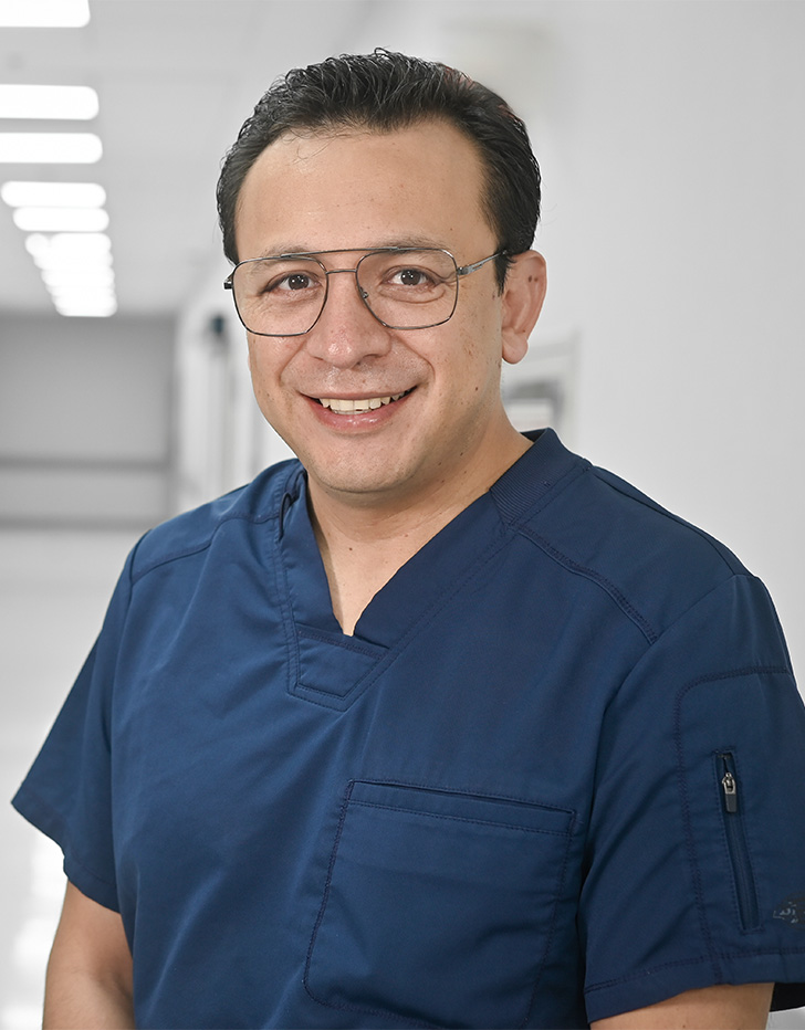 Es la foto de perfil de un urólogo en Ciudad de México de Hospital Angeles Universidad. Usa un uniforme médico azul y lentes. Tiene el cabello negro