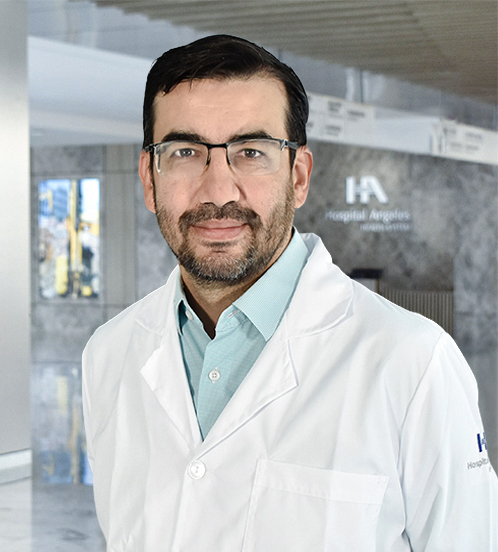 Es la foto de perfil de un ortopedista y traumatólogo en Querétaro de Hospital Angeles Centro-sur. Tiene el cabello y barba negro. Usa lentes con armazón negro, bata blanca y una camisa azul menta.