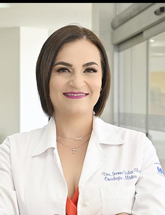 Es la foto de perfil de una oncóloga médica en Ciudad Juárez de Hospital Angeles Ciudad Juárez. Viste una bata blanca, blusa naranja, cabello corto y está sonriendo.