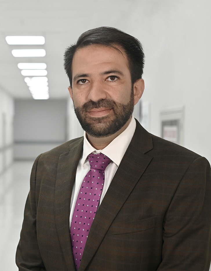 Es la foto de perfil de un cirujano neurológico en Ciudad de México de Hospital Angeles Universidad. Usa un saco negro, una camisa rosa palo y una corbata morada. Tiene el cabello y barba negro.