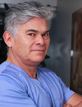 Es la foto de perfil de un ortopedista y traumatólogo en Ciudad de México de Hospital Angeles Universidad. Usa una camisa azul. Tiene el cabello gris y los brazos cruzados.