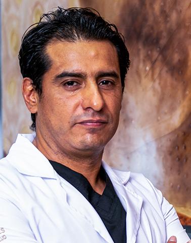 Es la foto de perfil de un cirujano general en León de Hospital Angeles León. Utiliza una bata blanca con una playera negra y tiene los brazos cruzados.