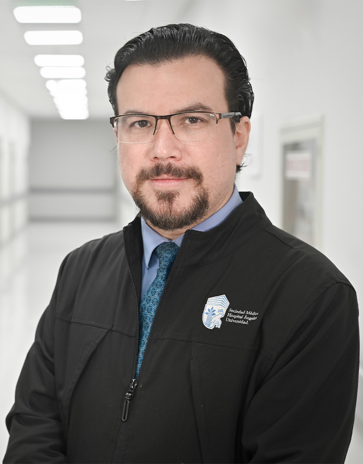Es la foto de perfil de un angiólogo y cirujano vascular en Ciudad de México de Hospital Angeles Universidad. Usa una chamarra negra, una camisa y corbata azul. Tiene el cabello y barba negra.