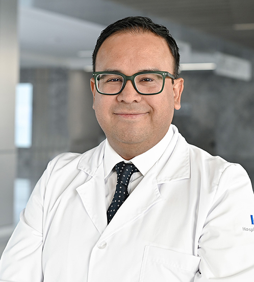 Es la foto de perfil de un cirujano general en Querétaro de Hospital Angeles Centro Sur. Usa una bata blanca con una camisa lila claro, y una corbata negra con puntos blancos.