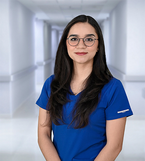 Joven doctora de lentes, pelo largo y uniforme azul posa en un pasillo de Hospital Angeles, la red más grande de México en salud privada. 