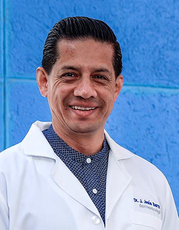 Es la foto de perfil de un gastroenterólogo en León de Hospital Angeles León. está sonriendo amablemente, tiene una bata blanca y una camisa azul marino con puntos blancos.