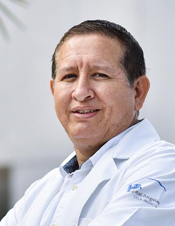 Es la foto de perfil de un oncólogo médico en Villahermosa de Hospital Angeles Villahermosa. Usa una bata y camisa blanca. Tiene el cabello negro. Está sonriendo y tiene los brazos cruzados.
