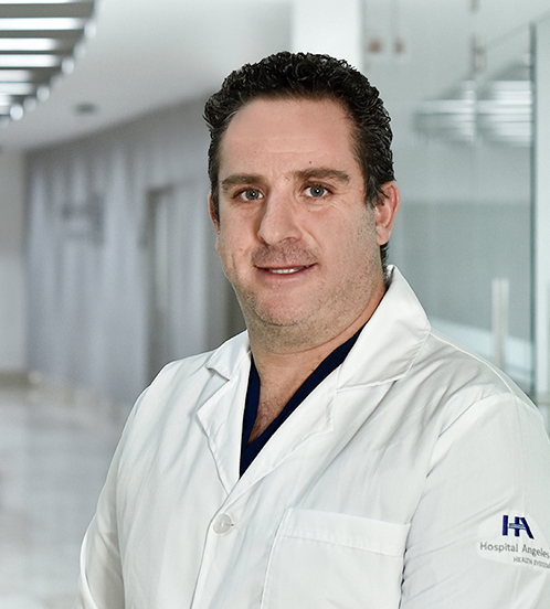 Es la foto de perfil de un inmunólogo y alergólogo pediátrico en Huixquilucan de Hospital Angeles Lomas. Usa una bata blanca, el fondo del pasillo es el hospital. El doctor es de tez blanca y cabello oscuro.