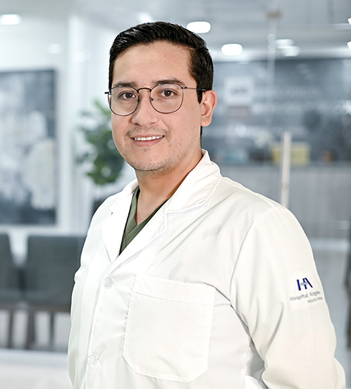 Especialista en Cardiología del Hospital Angeles Acoxpa Ciudad de México. Usa una bata blanca y un uniforme médico color verde. Tiene el cabello negro y usa lentes redondos.