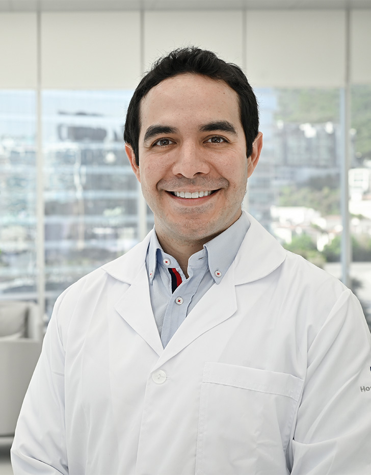 Es la foto de perfil de un dermatólogo en San Pedro Garza de Hospital Angeles Valle Oriente. Usa una bata blanca con una camisa gris. Tiene el cabello negro. Está sonriendo.